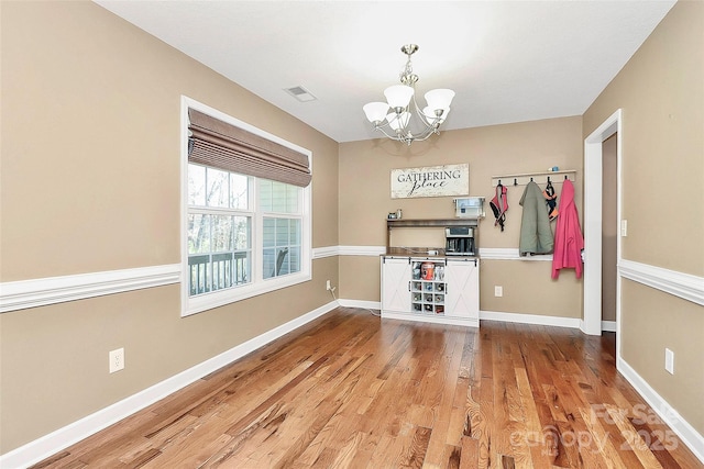 unfurnished dining area featuring a notable chandelier, visible vents, baseboards, and wood finished floors