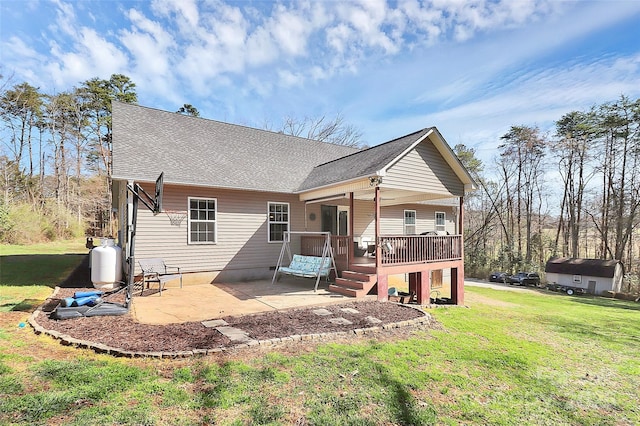 rear view of house with a deck, a lawn, a shingled roof, and a patio area