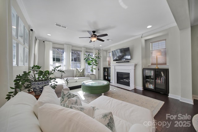 living area featuring visible vents, ornamental molding, a tiled fireplace, dark wood finished floors, and baseboards