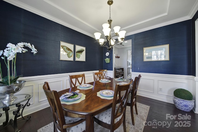 dining room with wallpapered walls, a decorative wall, wainscoting, wood finished floors, and a notable chandelier