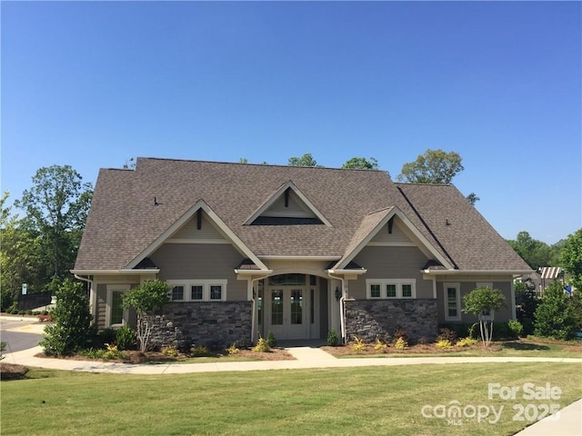 craftsman inspired home with french doors, stone siding, a front lawn, and a shingled roof