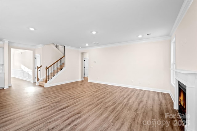 unfurnished living room featuring light wood finished floors, a warm lit fireplace, visible vents, stairs, and crown molding