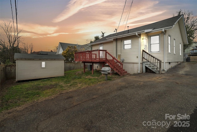 back of house featuring an outbuilding, fence, crawl space, a deck, and a storage shed