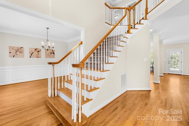 stairs with a notable chandelier, visible vents, wood finished floors, and ornamental molding