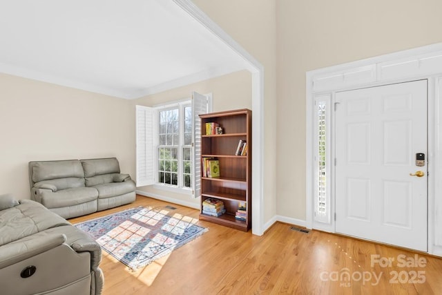 entrance foyer with ornamental molding, light wood-style floors, visible vents, and baseboards