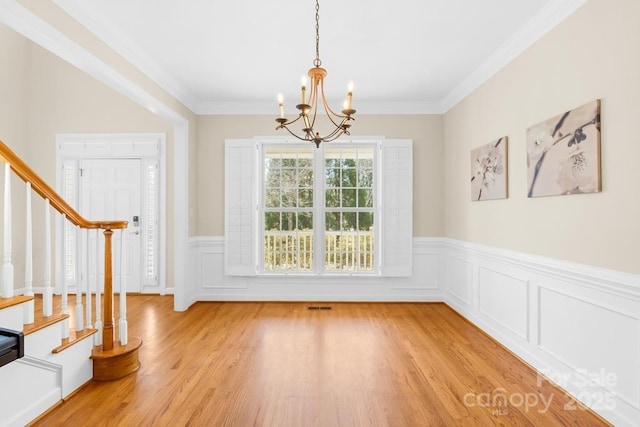 unfurnished dining area featuring an inviting chandelier, stairway, light wood-style floors, and crown molding