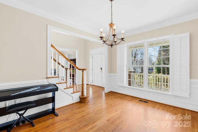 entryway featuring stairway, wood finished floors, visible vents, crown molding, and a chandelier