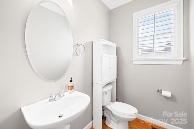 bathroom with toilet, wood finished floors, baseboards, and a sink