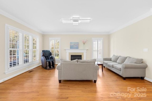 living area featuring a glass covered fireplace, plenty of natural light, light wood-type flooring, and ornamental molding