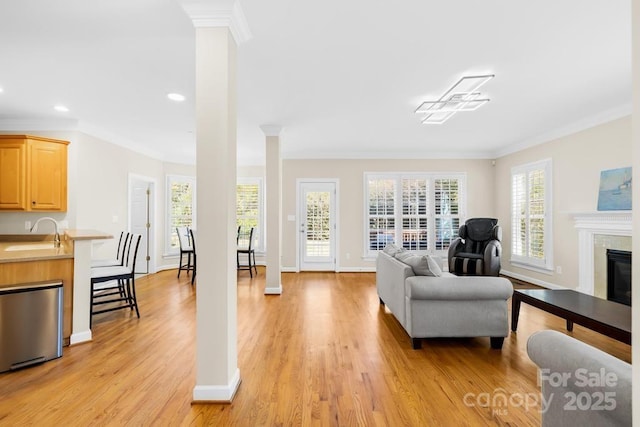 interior space featuring decorative columns, a glass covered fireplace, crown molding, and light wood finished floors