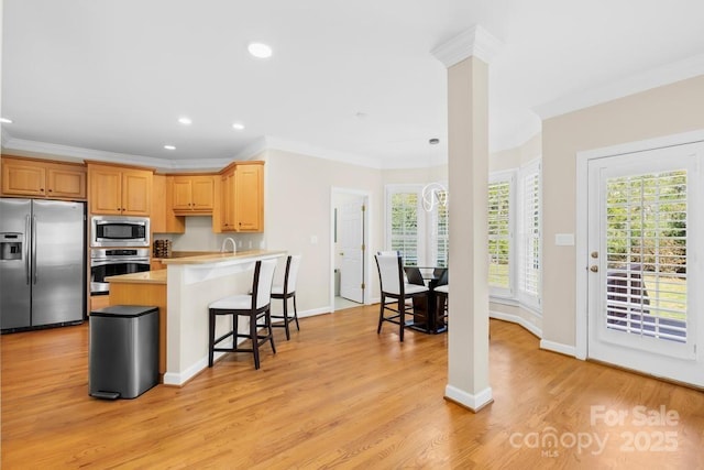 kitchen with light wood-type flooring, a breakfast bar, ornamental molding, a peninsula, and appliances with stainless steel finishes