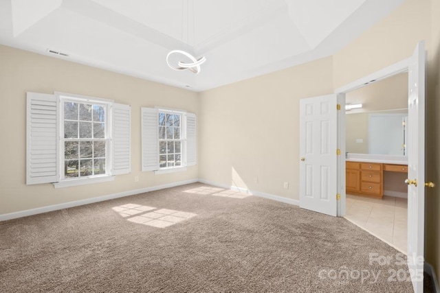 spare room featuring light carpet, a tray ceiling, and baseboards