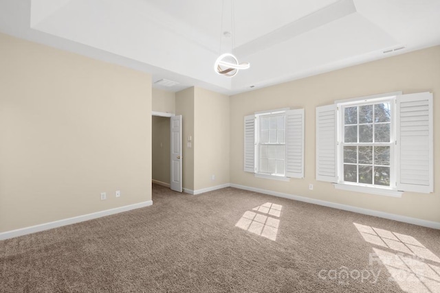 empty room with visible vents, baseboards, a tray ceiling, and carpet floors