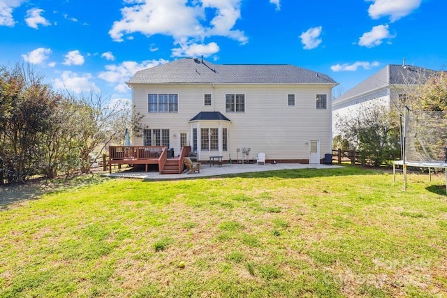 back of property with a yard, a deck, a patio, and a trampoline