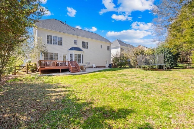 back of house featuring a trampoline, a deck, a lawn, and fence