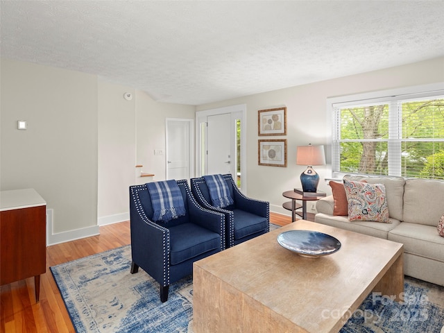 living area featuring baseboards, a textured ceiling, and light wood finished floors