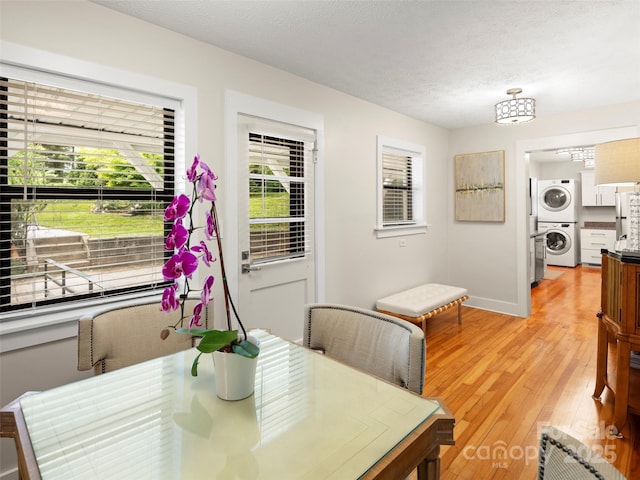 dining area featuring a textured ceiling, baseboards, stacked washer and clothes dryer, and light wood-type flooring