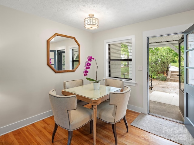 dining room with baseboards, light wood-type flooring, and a textured ceiling