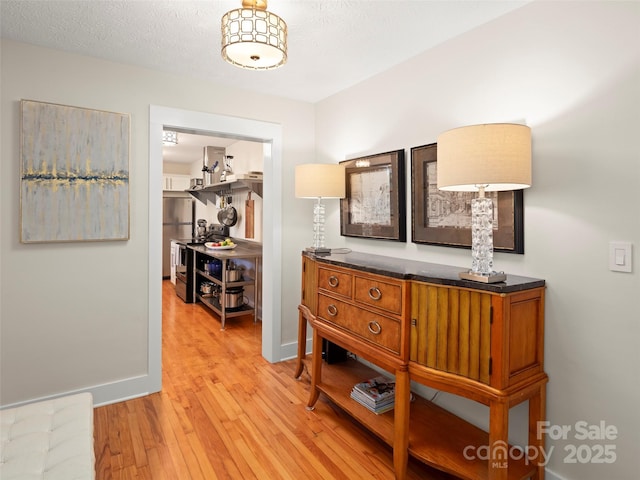 hall with light wood-style flooring, baseboards, and a textured ceiling