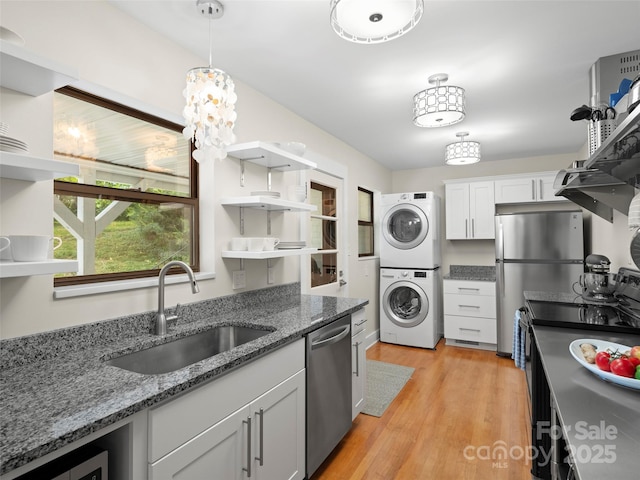 kitchen with stacked washer and clothes dryer, light wood-style flooring, a sink, open shelves, and stainless steel appliances