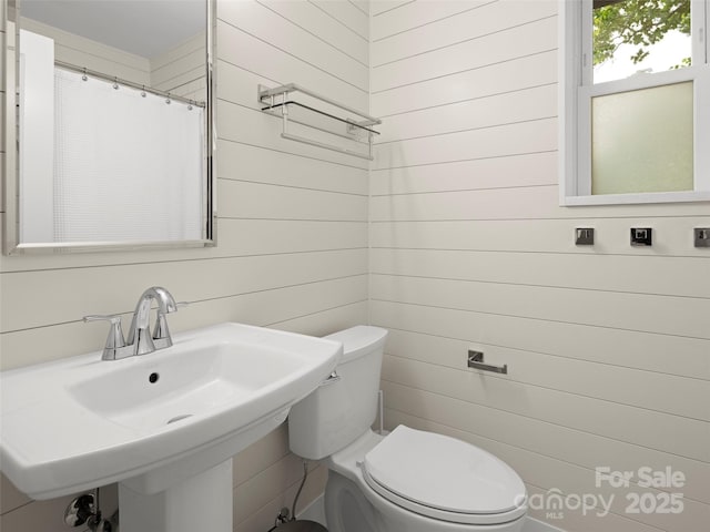 bathroom featuring a sink, a shower with curtain, toilet, and wood walls