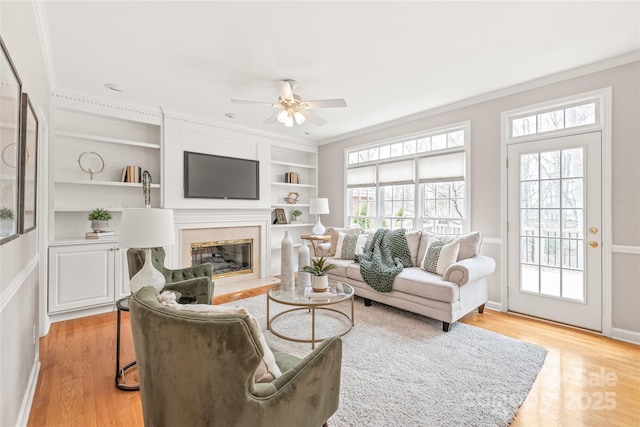 living room with built in features, a fireplace, light wood finished floors, and ornamental molding