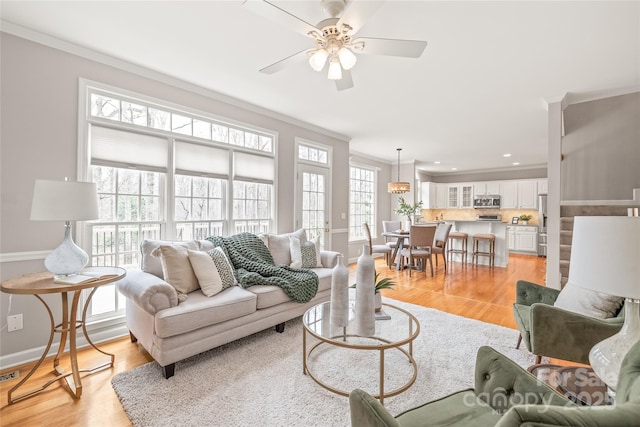 living area featuring baseboards, light wood-type flooring, crown molding, and ceiling fan