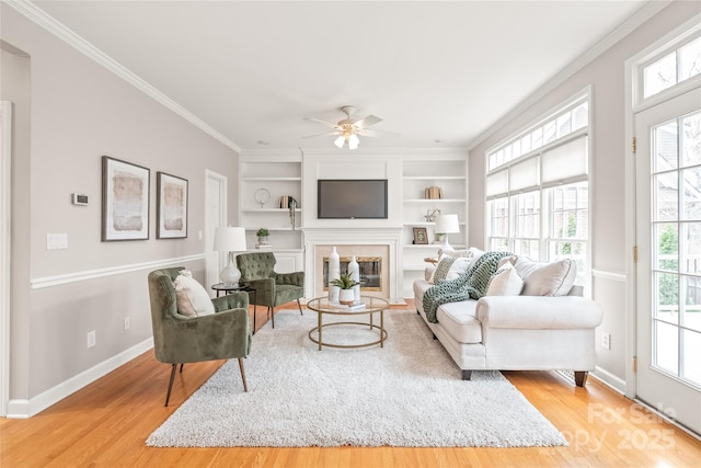 living area featuring built in shelves, wood finished floors, baseboards, a fireplace, and crown molding