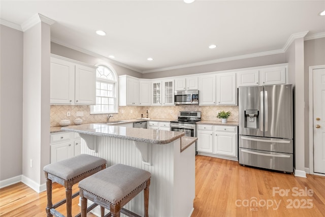 kitchen featuring a breakfast bar, ornamental molding, appliances with stainless steel finishes, white cabinetry, and light wood-type flooring