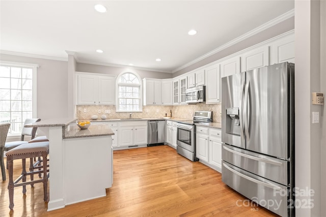 kitchen with a breakfast bar, appliances with stainless steel finishes, white cabinetry, crown molding, and backsplash