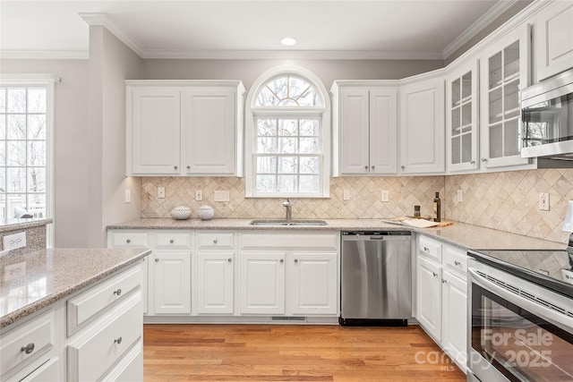 kitchen featuring a sink, stainless steel appliances, light wood-style floors, white cabinetry, and crown molding