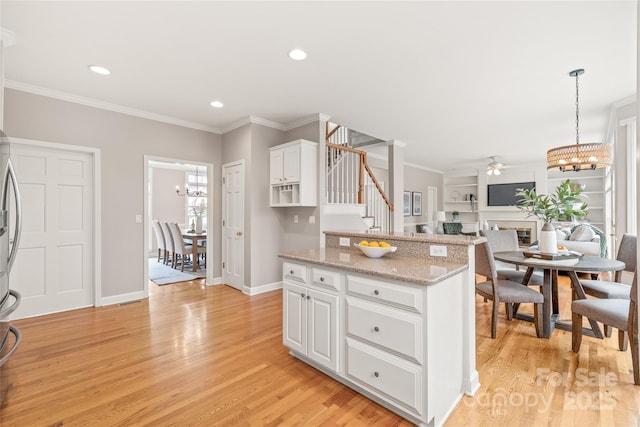 kitchen featuring light wood finished floors, white cabinets, crown molding, open floor plan, and a center island