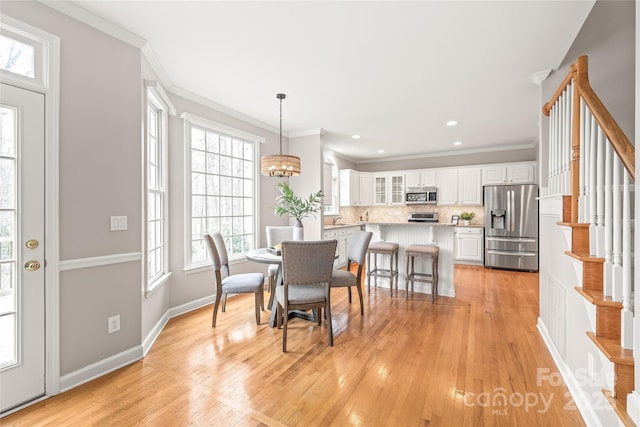 dining room with ornamental molding, light wood-style floors, baseboards, a chandelier, and stairs