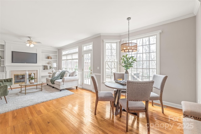 dining room with light wood-style flooring, built in features, a fireplace, crown molding, and baseboards