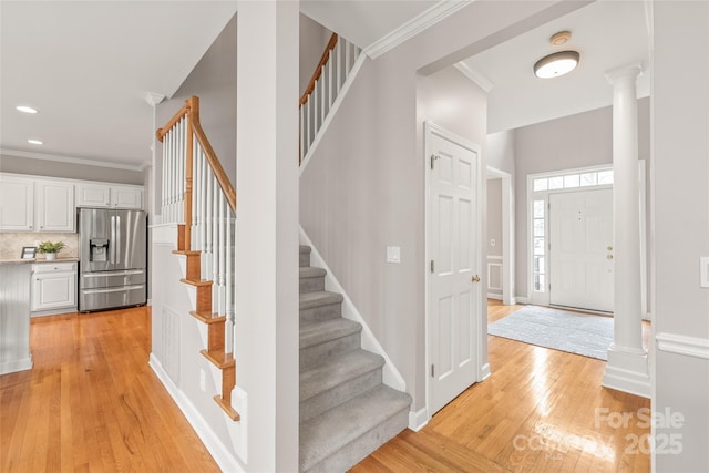 foyer with stairway, baseboards, ornate columns, light wood-style floors, and crown molding