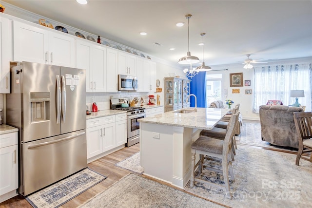 kitchen with a sink, stainless steel appliances, white cabinets, open floor plan, and light wood-type flooring