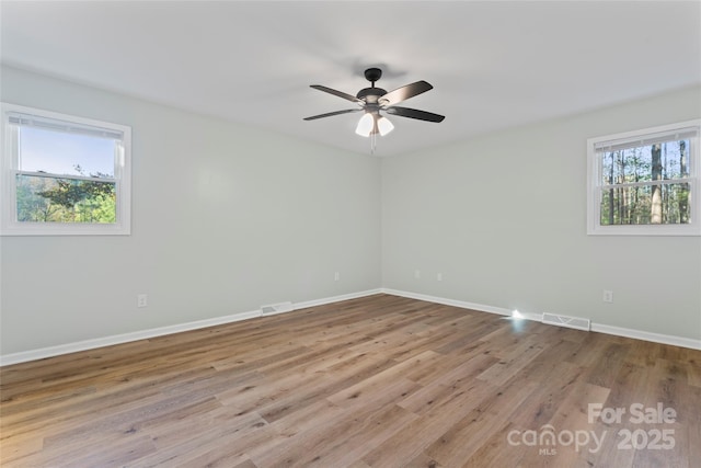 empty room featuring a healthy amount of sunlight, baseboards, and wood finished floors