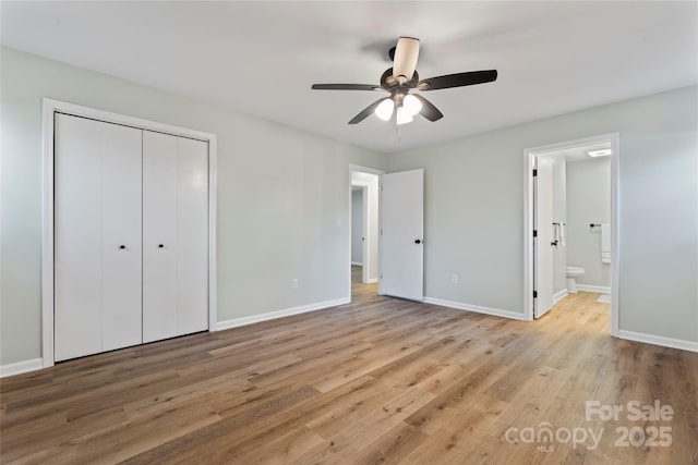 unfurnished bedroom with a closet, ensuite bathroom, baseboards, and wood finished floors