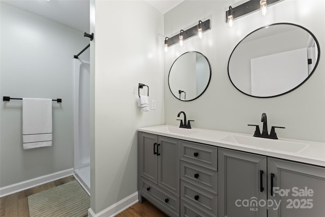 full bath featuring double vanity, wood finished floors, walk in shower, and a sink