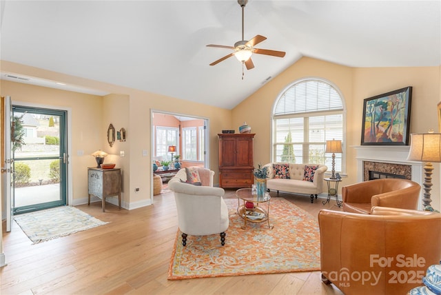 living area with light wood finished floors, lofted ceiling, a wealth of natural light, and a premium fireplace