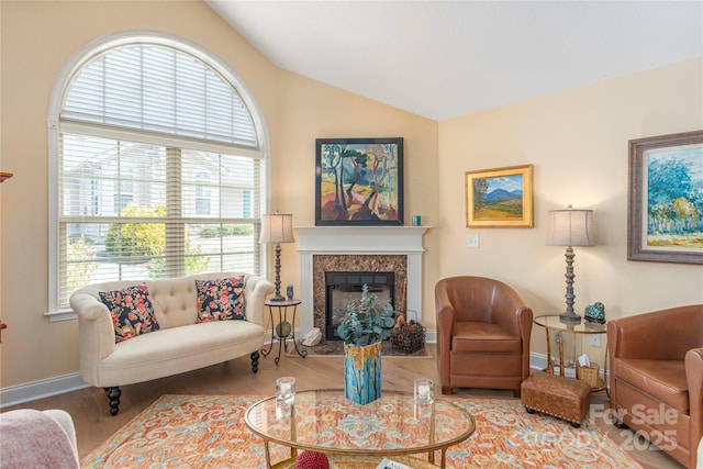 living room with a premium fireplace, lofted ceiling, baseboards, and wood finished floors