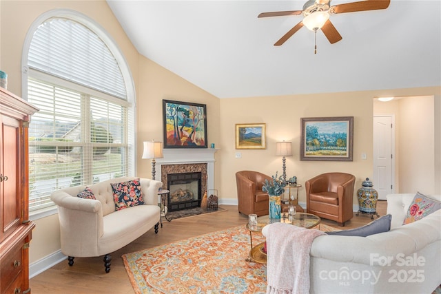 living room with ceiling fan, a premium fireplace, baseboards, and wood finished floors