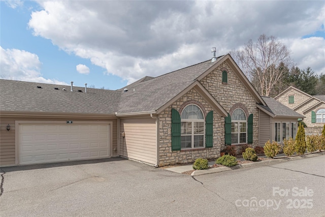 view of front of house featuring aphalt driveway, a garage, stone siding, and roof with shingles