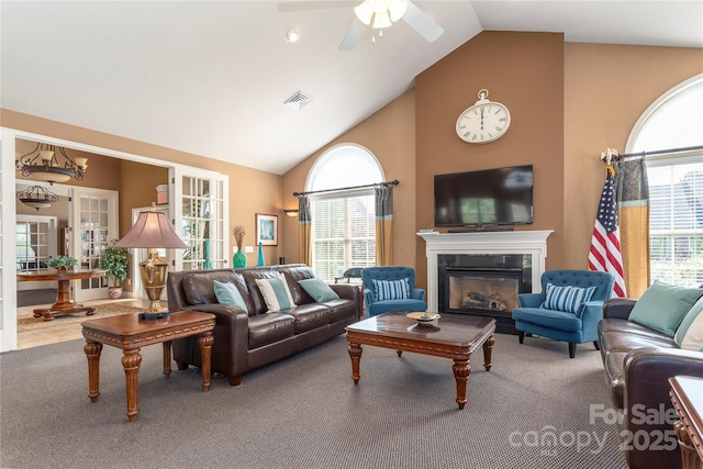 living room with visible vents, ceiling fan, carpet flooring, a glass covered fireplace, and high vaulted ceiling