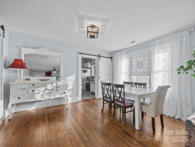 dining area featuring a textured ceiling, a barn door, and hardwood / wood-style floors