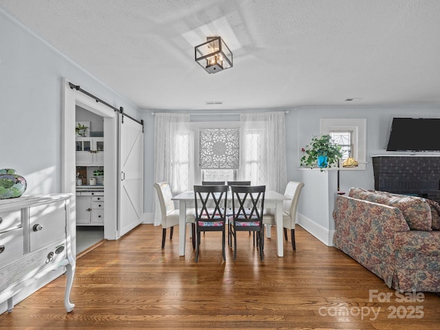 dining space featuring baseboards, a textured ceiling, a barn door, and wood finished floors