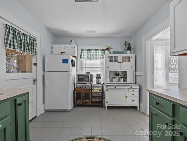 kitchen featuring visible vents, green cabinetry, freestanding refrigerator, white cabinetry, and stainless steel microwave