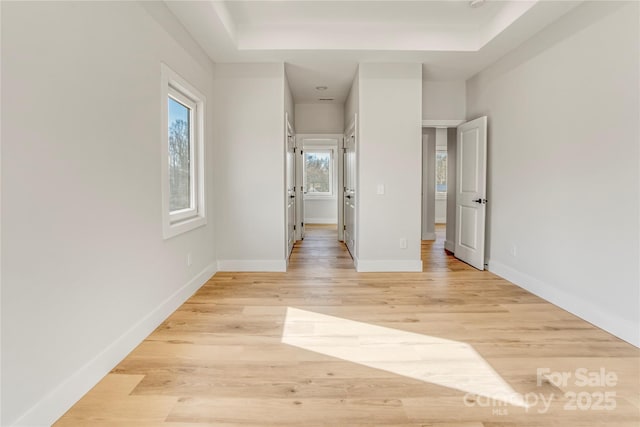 interior space with a raised ceiling, light wood-style floors, and baseboards