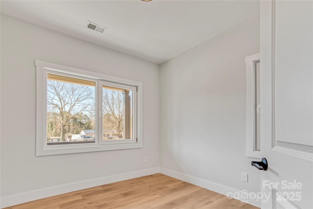 empty room with light wood finished floors, visible vents, and baseboards