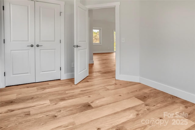 unfurnished bedroom featuring a closet, light wood-style flooring, and baseboards